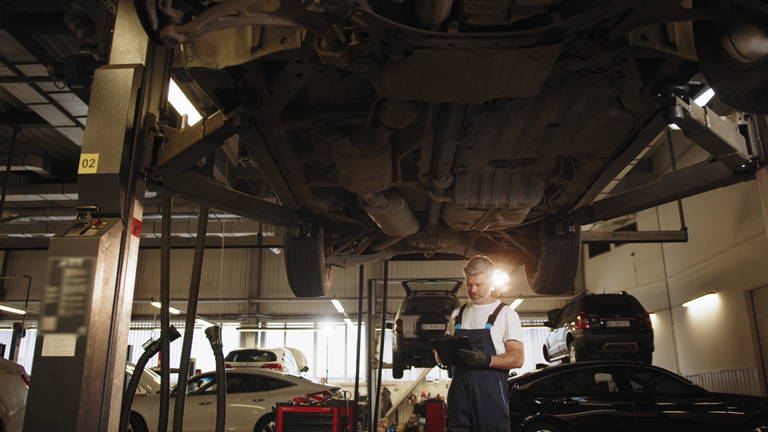 professional middle aged car mechanic taking notes under vehicle at auto repair shop, Garage Liability